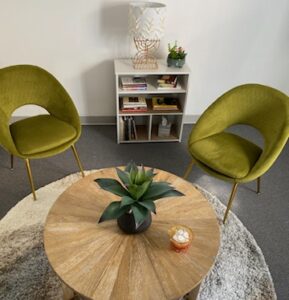 meeting room comfortably decorated with midcentury modern green chairs and a bleached wood sunburst coffee table with a white bookcase in the rear